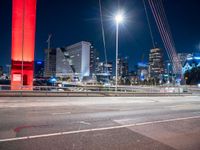 the city skyline is illuminated at night from under the bridge on a street in front of the road is a busy highway