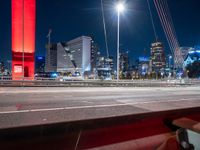 the city skyline is illuminated at night from under the bridge on a street in front of the road is a busy highway