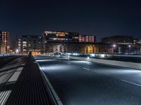 a road in the city with many lights shining at night time, seen from across an empty highway