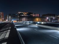 a road in the city with many lights shining at night time, seen from across an empty highway