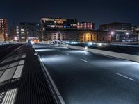 a road in the city with many lights shining at night time, seen from across an empty highway