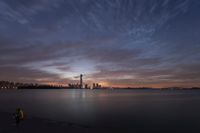 man looking out over a large body of water with a city in the background at dusk