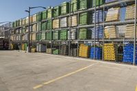 containers with water and plastic are piled high on a rack in a parking lot near a fence