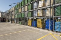 containers with water and plastic are piled high on a rack in a parking lot near a fence