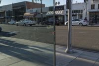 some cars and people on a city street and traffic signals and cars parked in front