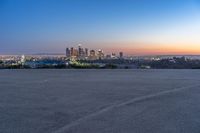 a city at dusk and a lone bench in front of it in the field of gravel