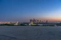 a city at dusk and a lone bench in front of it in the field of gravel