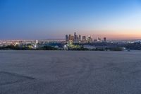 a city at dusk and a lone bench in front of it in the field of gravel