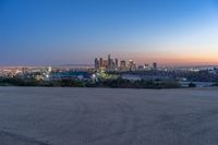 a city at dusk and a lone bench in front of it in the field of gravel