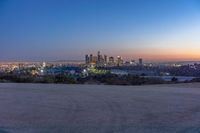 a city at dusk and a lone bench in front of it in the field of gravel