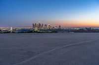 a city at dusk and a lone bench in front of it in the field of gravel