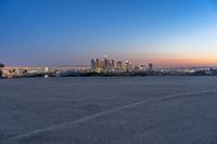 a city at dusk and a lone bench in front of it in the field of gravel