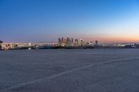 a city at dusk and a lone bench in front of it in the field of gravel
