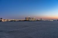 a city at dusk and a lone bench in front of it in the field of gravel