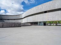 a circular concrete structure with blue sky and clouds above it in the background, there are people walking through the area