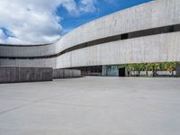 a circular concrete structure with blue sky and clouds above it in the background, there are people walking through the area