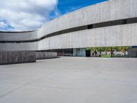 a circular concrete structure with blue sky and clouds above it in the background, there are people walking through the area