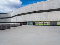 a circular concrete structure with blue sky and clouds above it in the background, there are people walking through the area