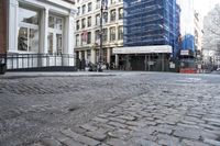 brick road surrounded by tall buildings in city area with cars parked on it's side
