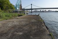 the walkway extends over to a bridge near the river with buildings in the background and water on either side