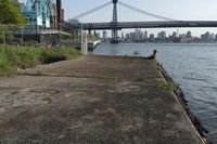 the walkway extends over to a bridge near the river with buildings in the background and water on either side