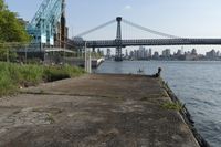 the walkway extends over to a bridge near the river with buildings in the background and water on either side