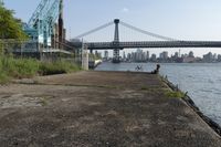 the walkway extends over to a bridge near the river with buildings in the background and water on either side