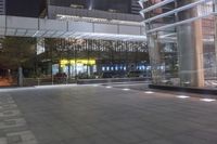 a walkway outside a large building at night with many lights on it and cars parked by the side of the street