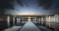 a long pool is in between buildings with a sky background at night time and there are clouds overhead