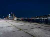 a long sidewalk that is beside water and buildings near it, with the moon in the background