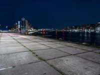 a long sidewalk that is beside water and buildings near it, with the moon in the background