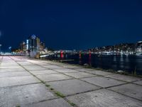 a long sidewalk that is beside water and buildings near it, with the moon in the background