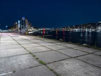 a long sidewalk that is beside water and buildings near it, with the moon in the background