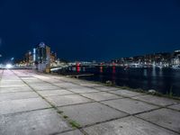 a long sidewalk that is beside water and buildings near it, with the moon in the background