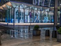 an outside area with several plants and benches next to an awning at night and light reflections on the pavement