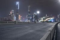 an empty highway through an urban area at night with lights above it and a city skyline in the distance