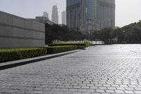 a large brick area next to a park in a city setting with buildings on either side