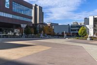 an empty courtyard in front of many buildings and trees in the middle of town, with a bench on a sidewalk