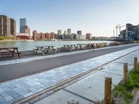 many benches line the edge of a bridge overlooking a city river and a body of water