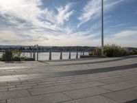 the view of the river and the sidewalk with a skateboarder on it in a city