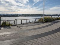 the view of the river and the sidewalk with a skateboarder on it in a city