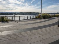 the view of the river and the sidewalk with a skateboarder on it in a city