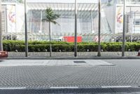 a street in front of a building with an open metal grill in it and people walking along the sidewalk