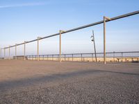 a parking lot with metal poles and fence surrounding it with water on the beach in the distance