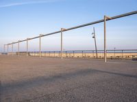 a parking lot with metal poles and fence surrounding it with water on the beach in the distance