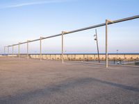 a parking lot with metal poles and fence surrounding it with water on the beach in the distance