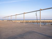 a parking lot with metal poles and fence surrounding it with water on the beach in the distance