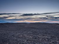 a very dark desert with some sand and bushes around it at sunset, near the horizon