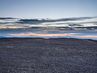 a very dark desert with some sand and bushes around it at sunset, near the horizon