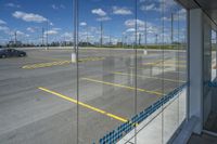 an empty parking lot with a car parked nearby through the glass door of one of the terminal